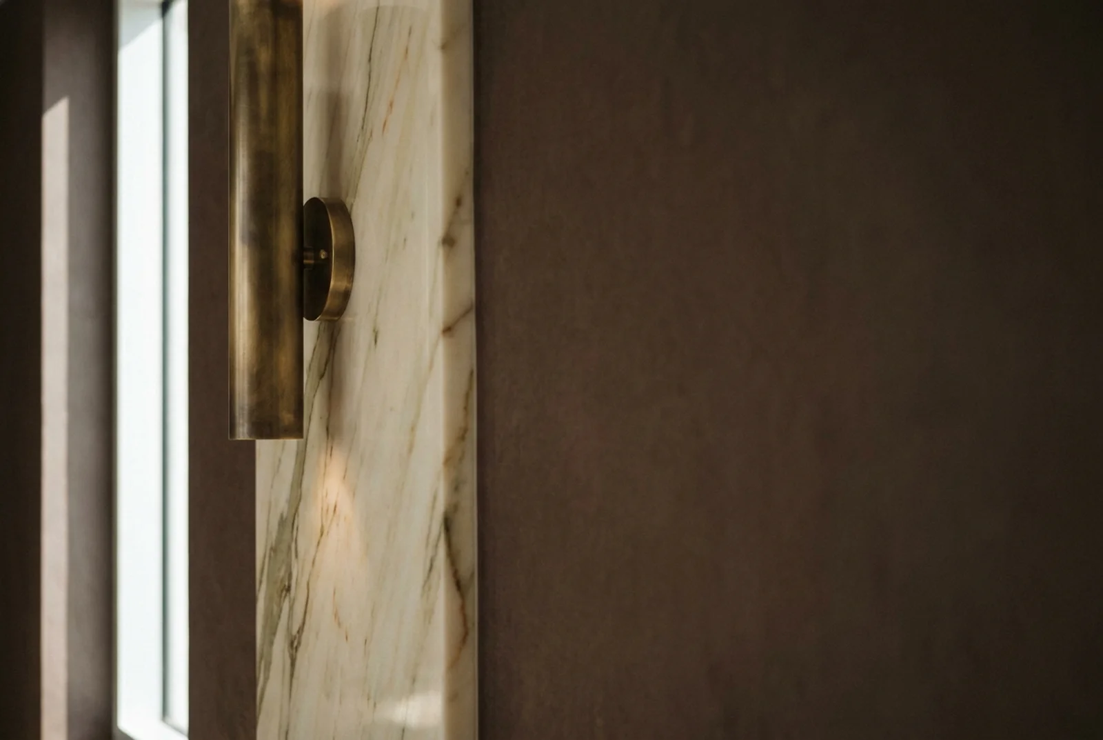 Architectural detail of a luxury interior: marble wall with subtle veining, brass fixture catching afternoon light, representing the category Antonovich Design operates in